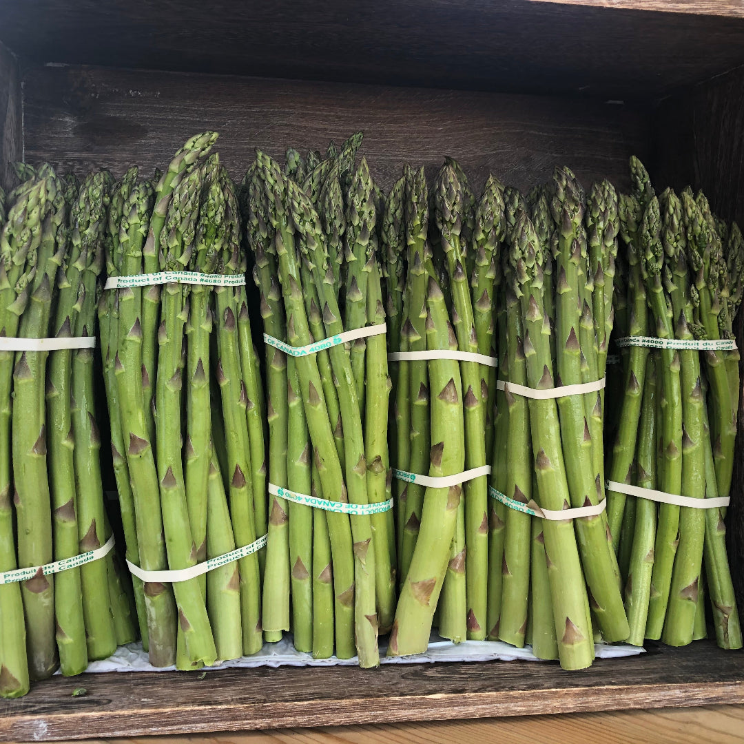 Bundles of green asparagus tied with rubber bands inside a wooden crate.